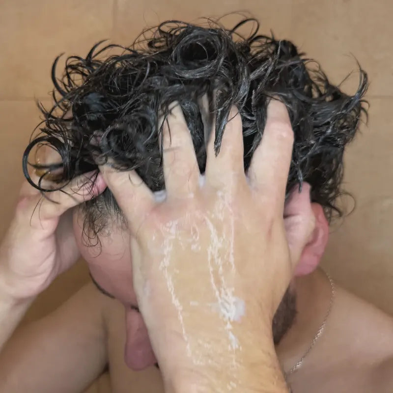 Man using tea tree conditioner in his hair inside the shower