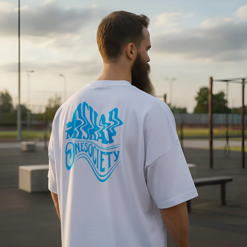 Man wearing a white t-shirt with blue graphics and text, standing outdoors.