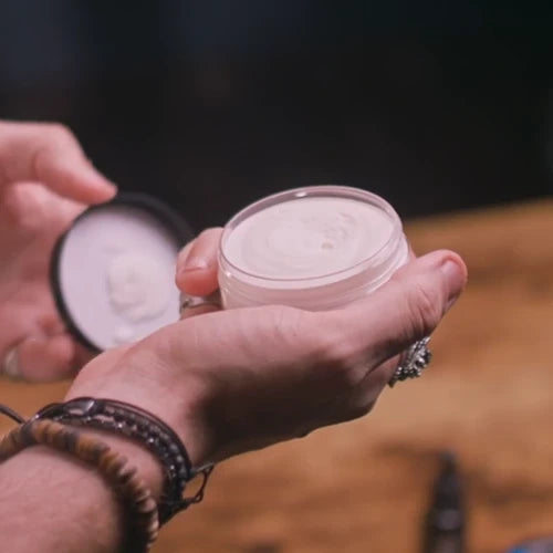 Person holding a beard butter container of cream with a blurred background