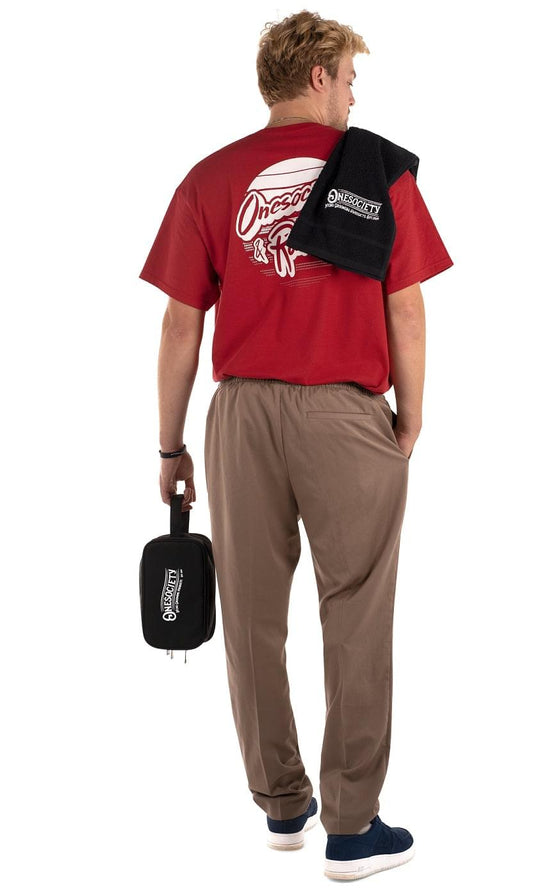 A man wearing a stylish red T-shirt holds a One Society Men's Grooming Products wash bag in one hand and a soft cotton towel in the other. Onesociety Gym Bag