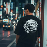 Person wearing a black t-shirt with 'Onesociety & Rockwood' design in an urban night setting.