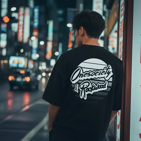 Person wearing a black t-shirt with 'Onesociety & Rockwood' design in an urban night setting.
