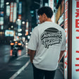 Person wearing a white t-shirt with text on the back in an urban night setting.