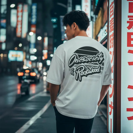 Person wearing a white t-shirt with text on the back in an urban night setting.
