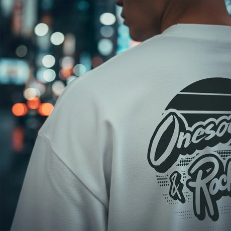 Person wearing a white t-shirt with a brand logo on the back against a blurred cityscape background