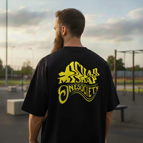 Man wearing a black t-shirt with yellow graphics and text, standing outdoors.