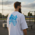 Man wearing a white t-shirt with blue graphics and text, standing outdoors.