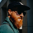 Person with a beard wearing sunglasses against an urban background