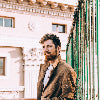 Man with beard leaning on a fence