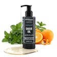 A bottle of Onesociety Peppermint & Lemon Shave Oil stands on a reflective gold base, surrounded by fresh mint leaves, whole oranges, and orange peels on a clean white background.