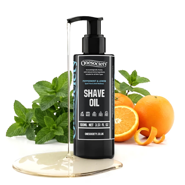 A bottle of Onesociety Peppermint & Lemon Shave Oil stands on a reflective gold base, surrounded by fresh mint leaves, whole oranges, and orange peels on a clean white background.